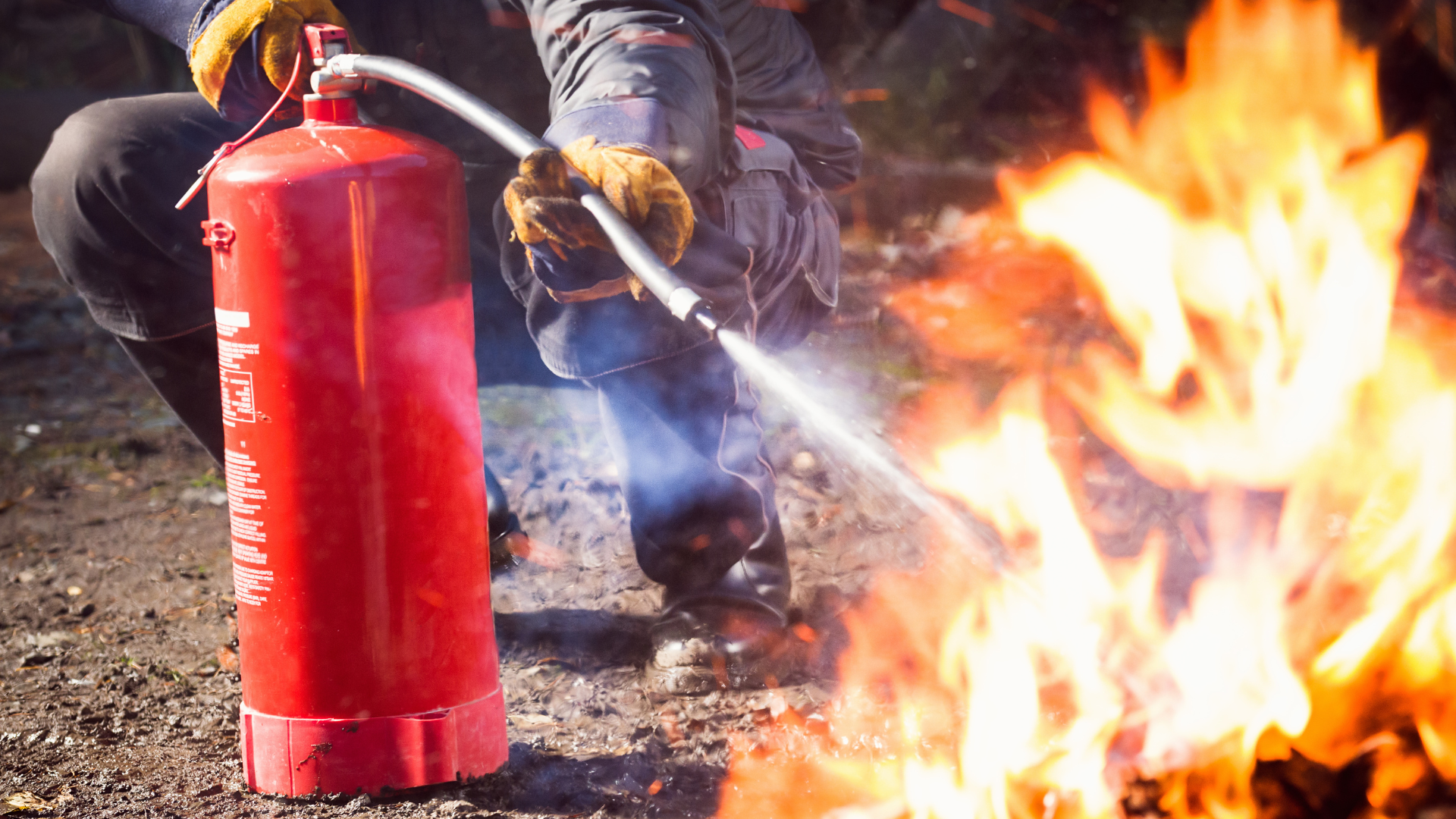 Personnel de sécurité utilisant un extincteur rouge pour éteindre un feu en extérieur.